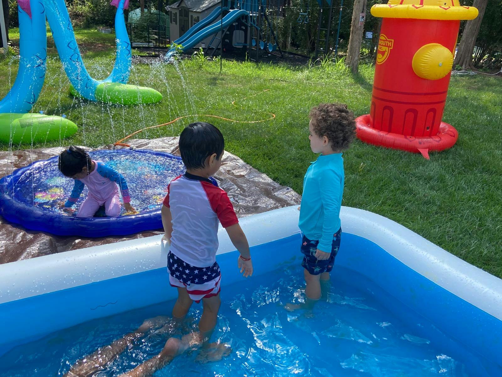 Children playing in small pools and a sprinkler in a backyard