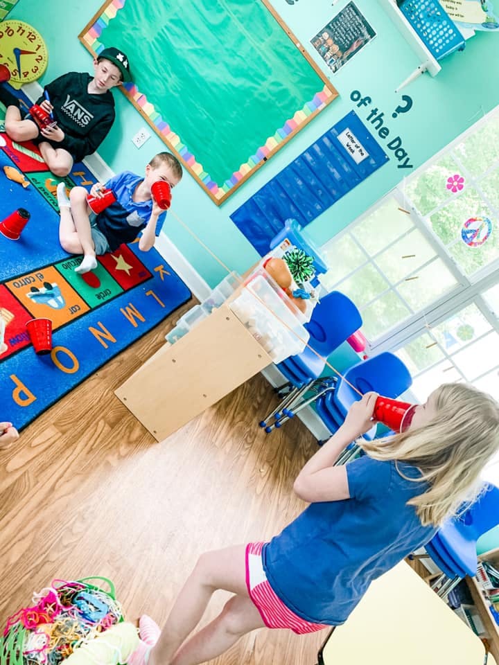 Three children playing with red cups in a classroom