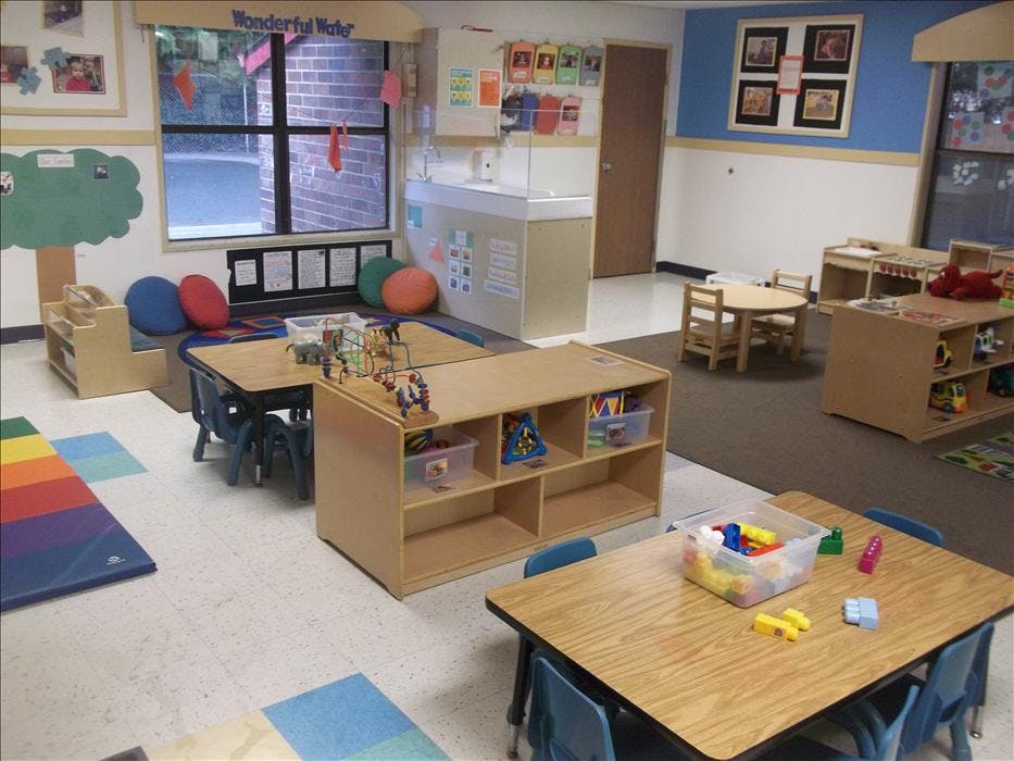 A colorful classroom with small tables, chairs, and shelves filled with toys