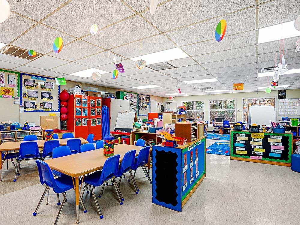 Empty classroom with small tables and blue chairs, colorful decorations hanging from the ceiling