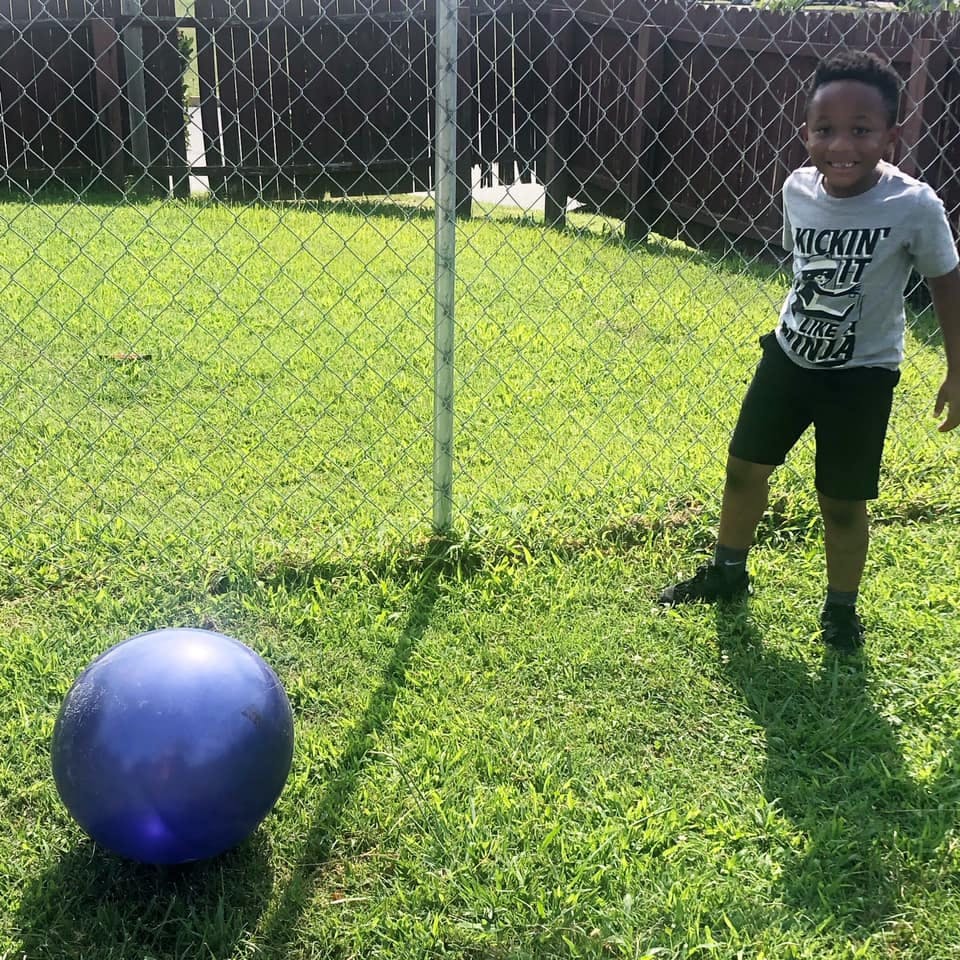 Child standing on grass next to a large blue ball