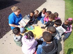 Adult reading a book to a group of children sitting in a circle outdoors
