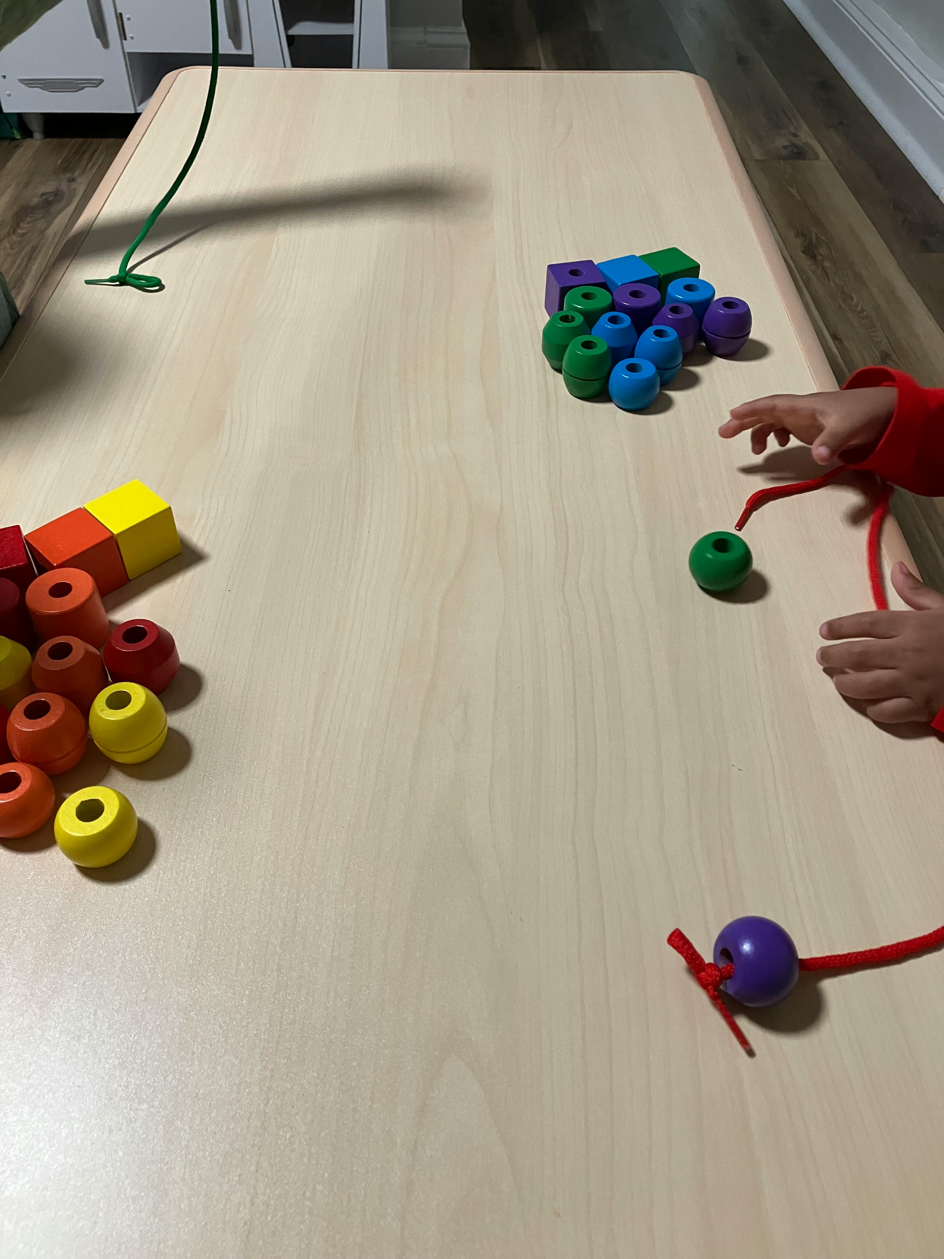 Child's hands playing with beads and string on a table