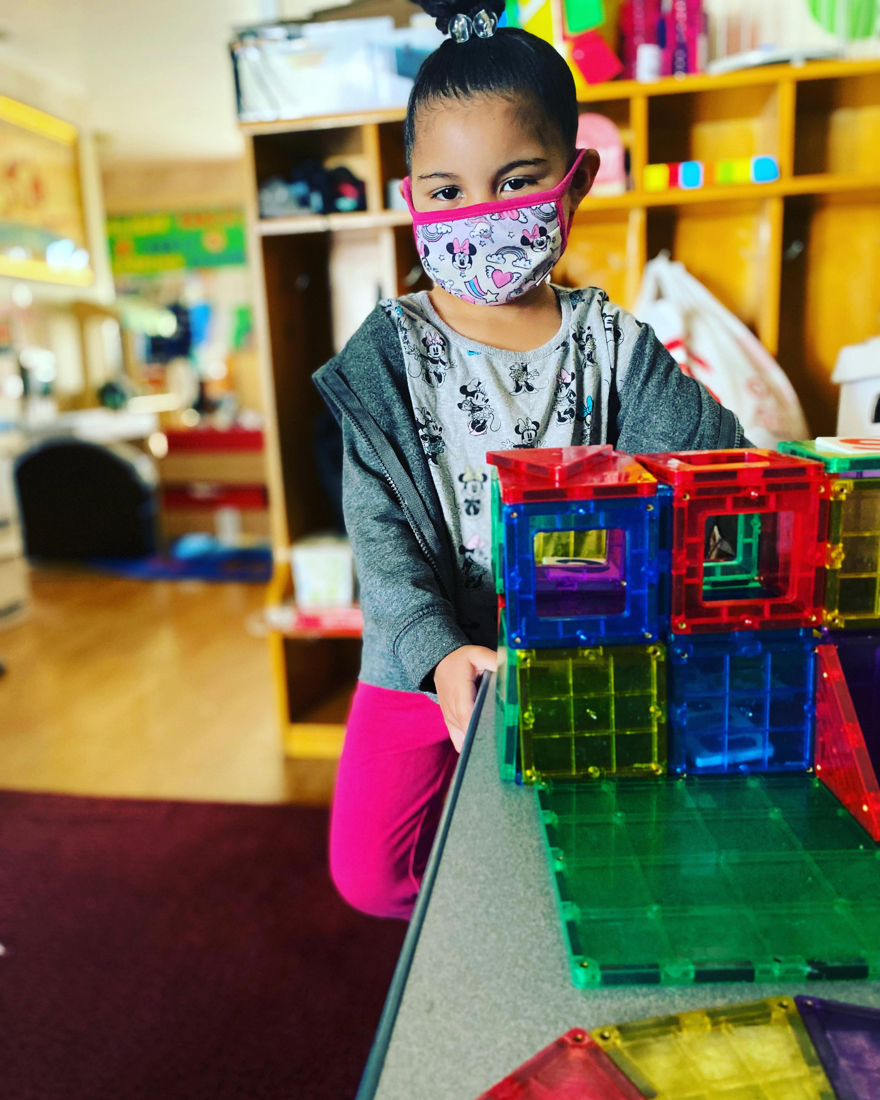 Child in a mask playing with colorful magnetic blocks