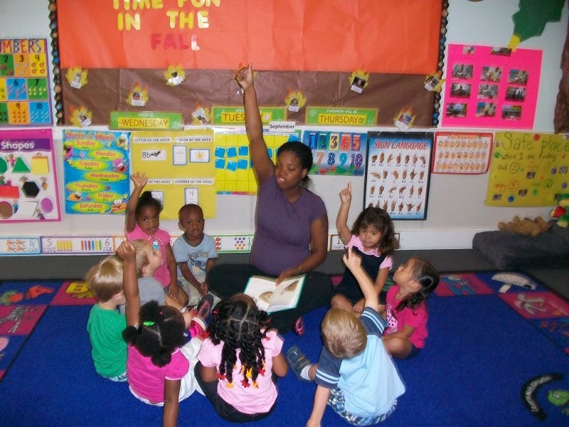 Person reading to children in a classroom, some children raising hands