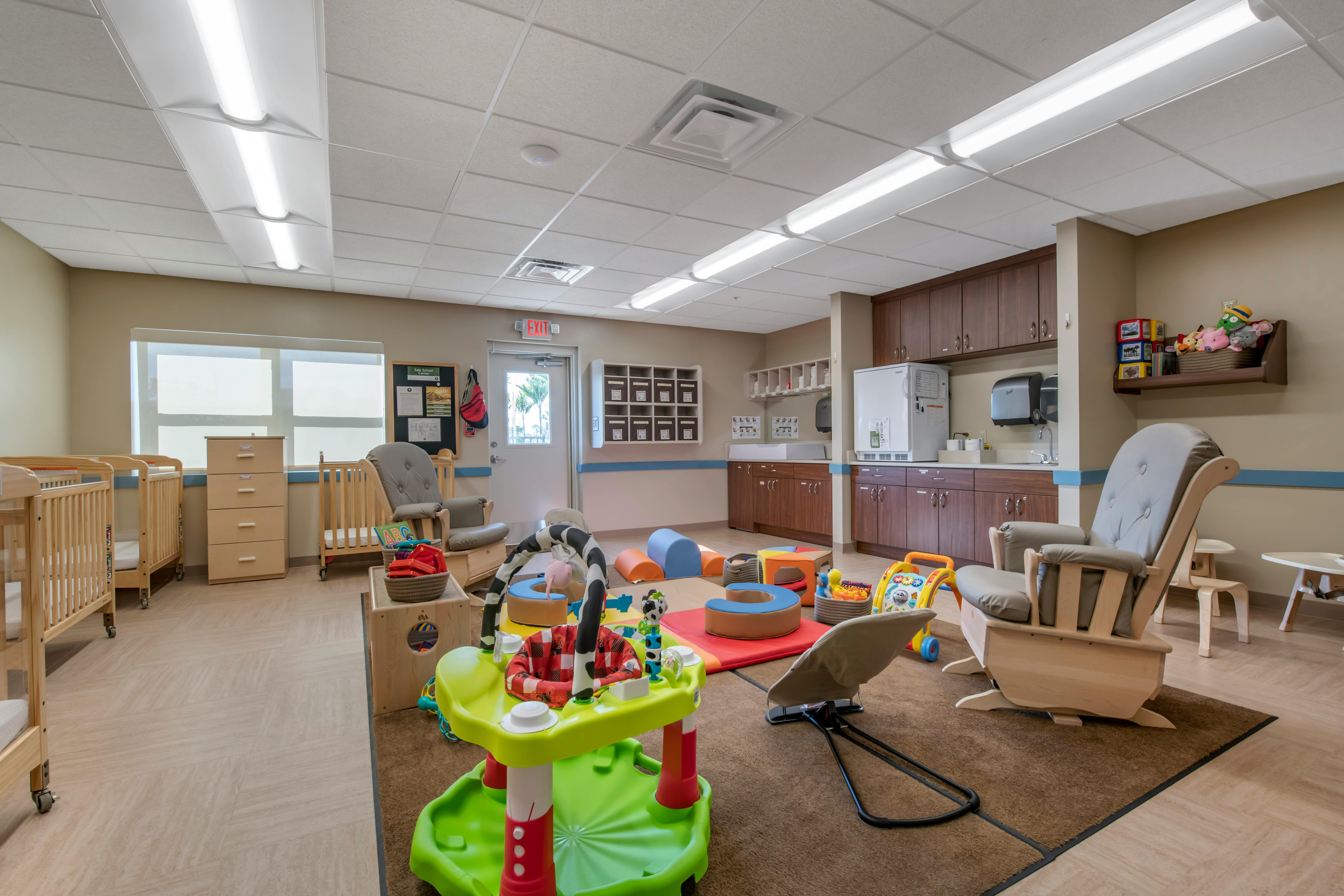 Childcare room with cribs, play mats, interactive toys, and a changing station