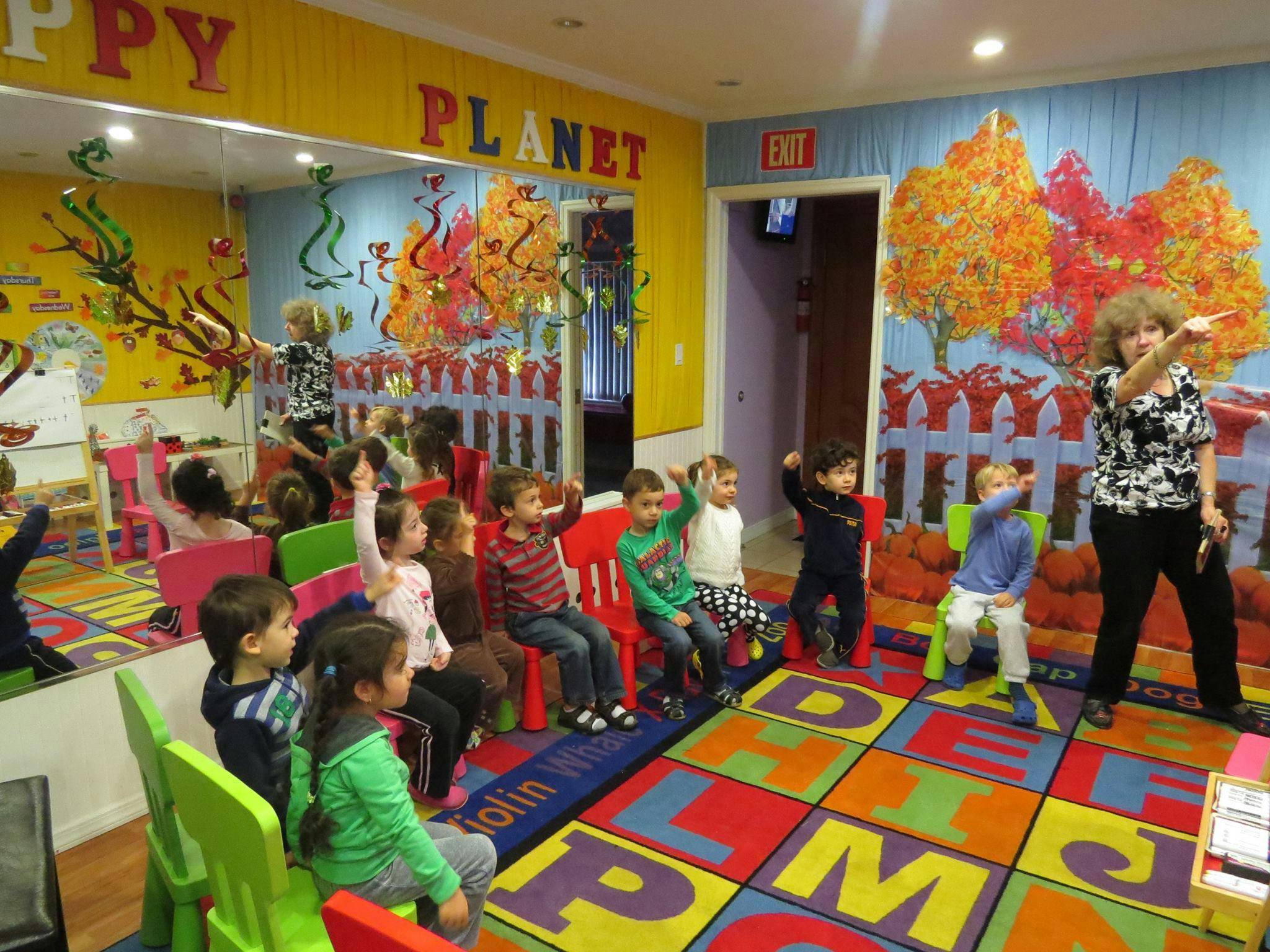 Adult and children in a classroom, some children raising hands