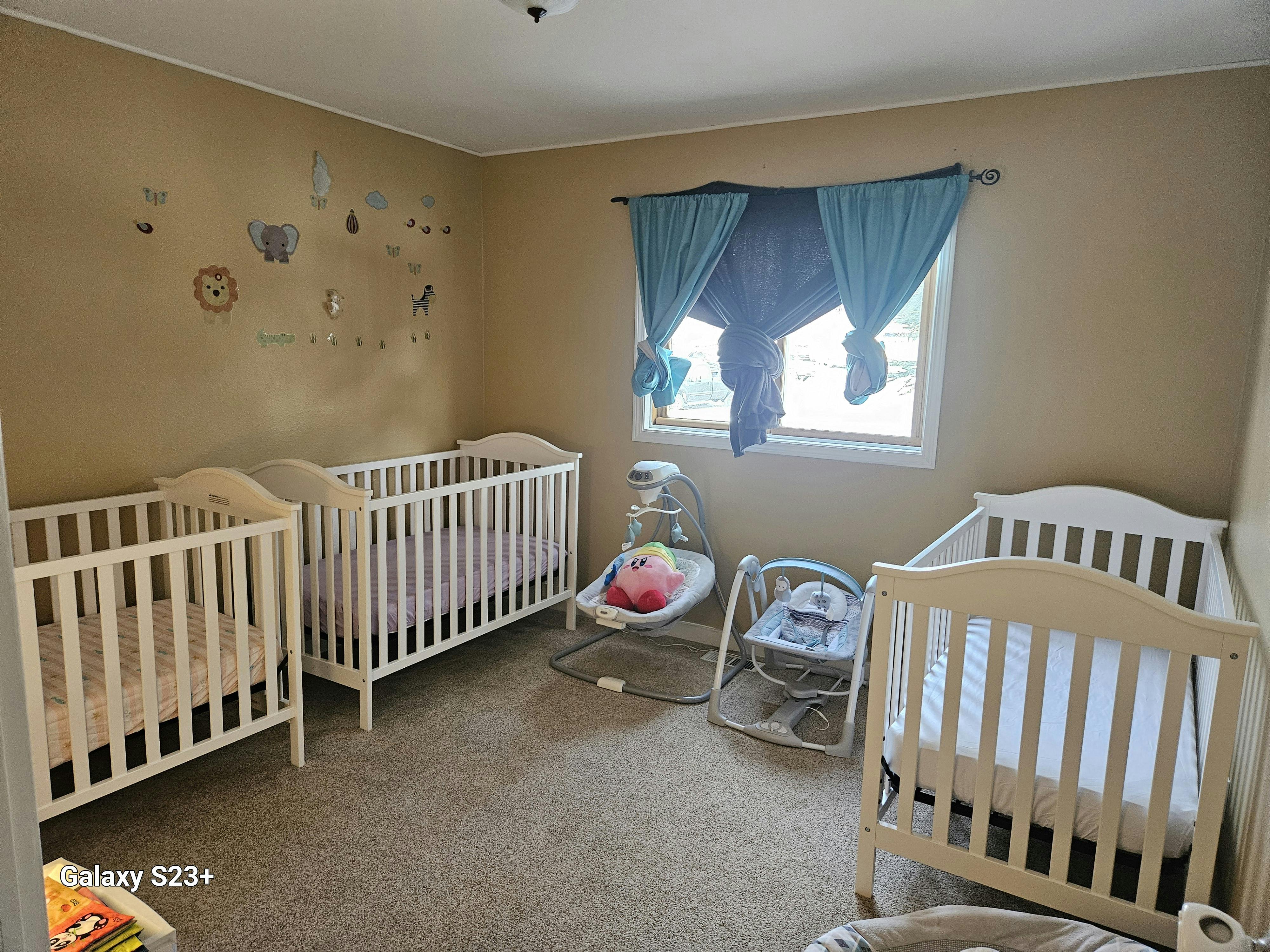 Three white cribs and two baby swings in a room