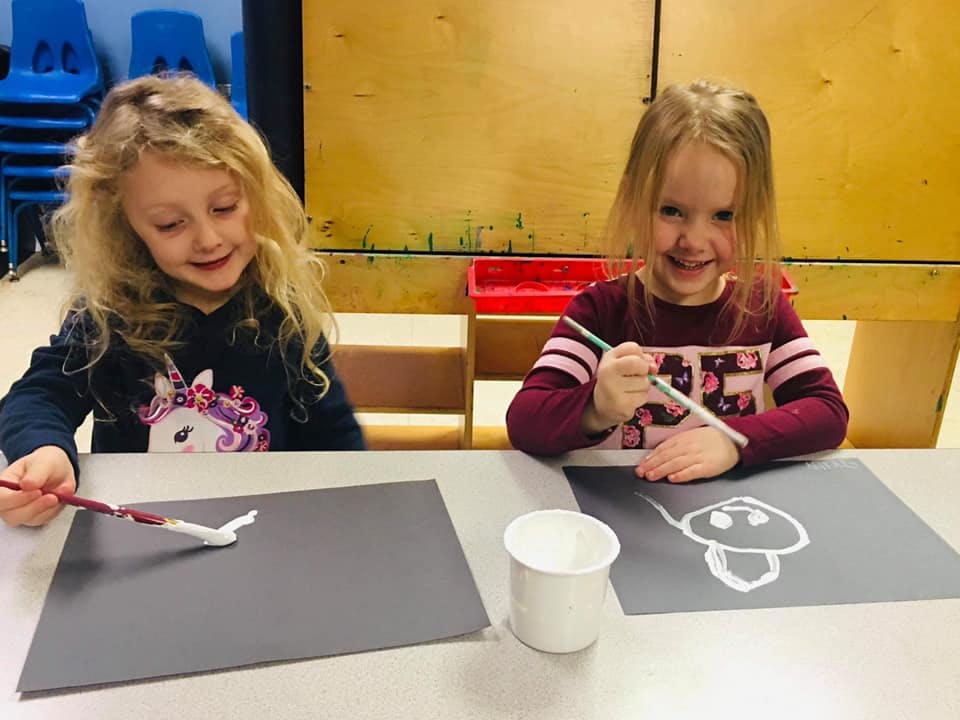 Two children painting on paper at a table