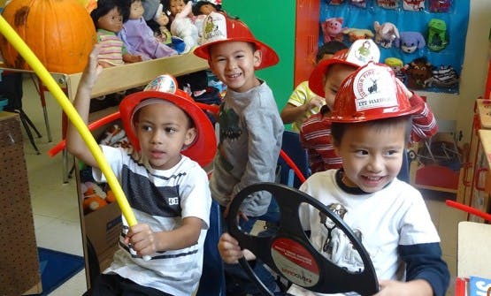 Three children wearing firefighter hats playing in a classroom