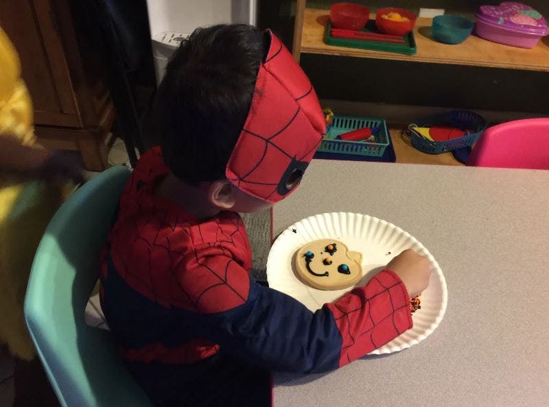 Child in Spider-Man costume eating a cookie from a paper plate