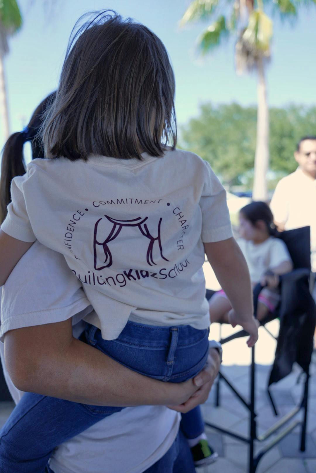 Person holding a child wearing a BuildingKidzSchool shirt