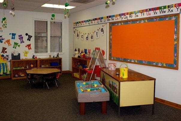 Classroom with small tables, shelves, and a large orange bulletin board