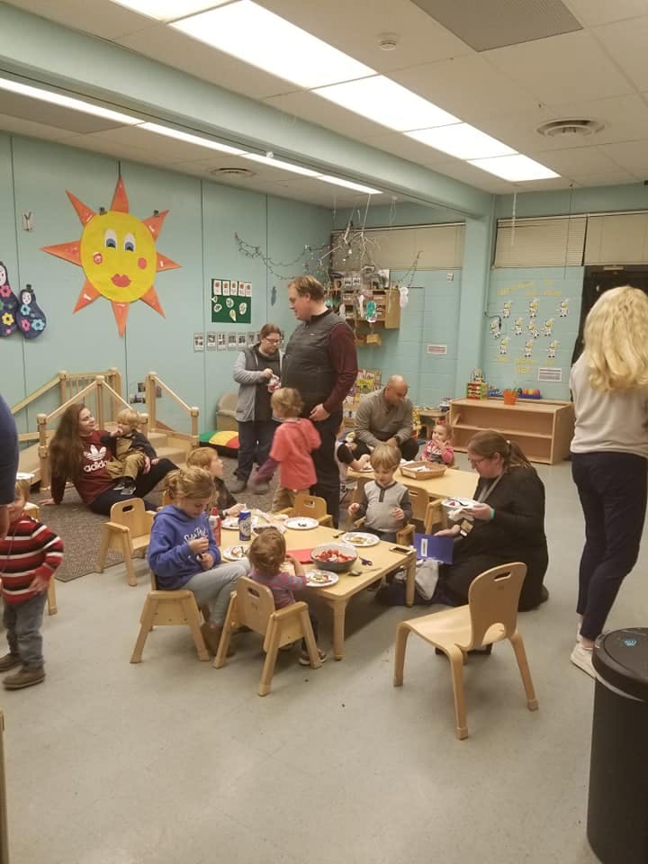 Adults and children gathered in a room with small tables and chairs