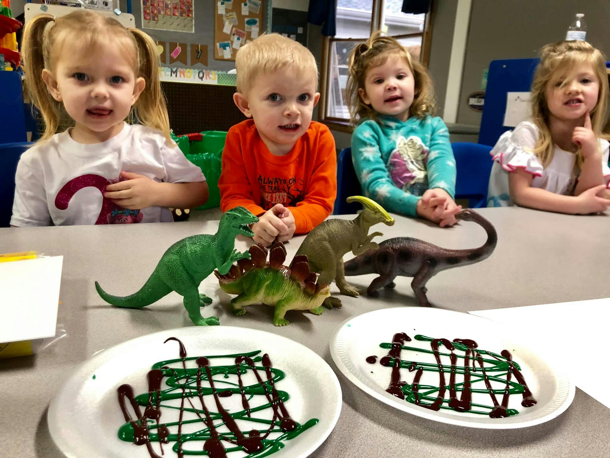 Children at a table with dinosaur toys and plates with green and brown icing