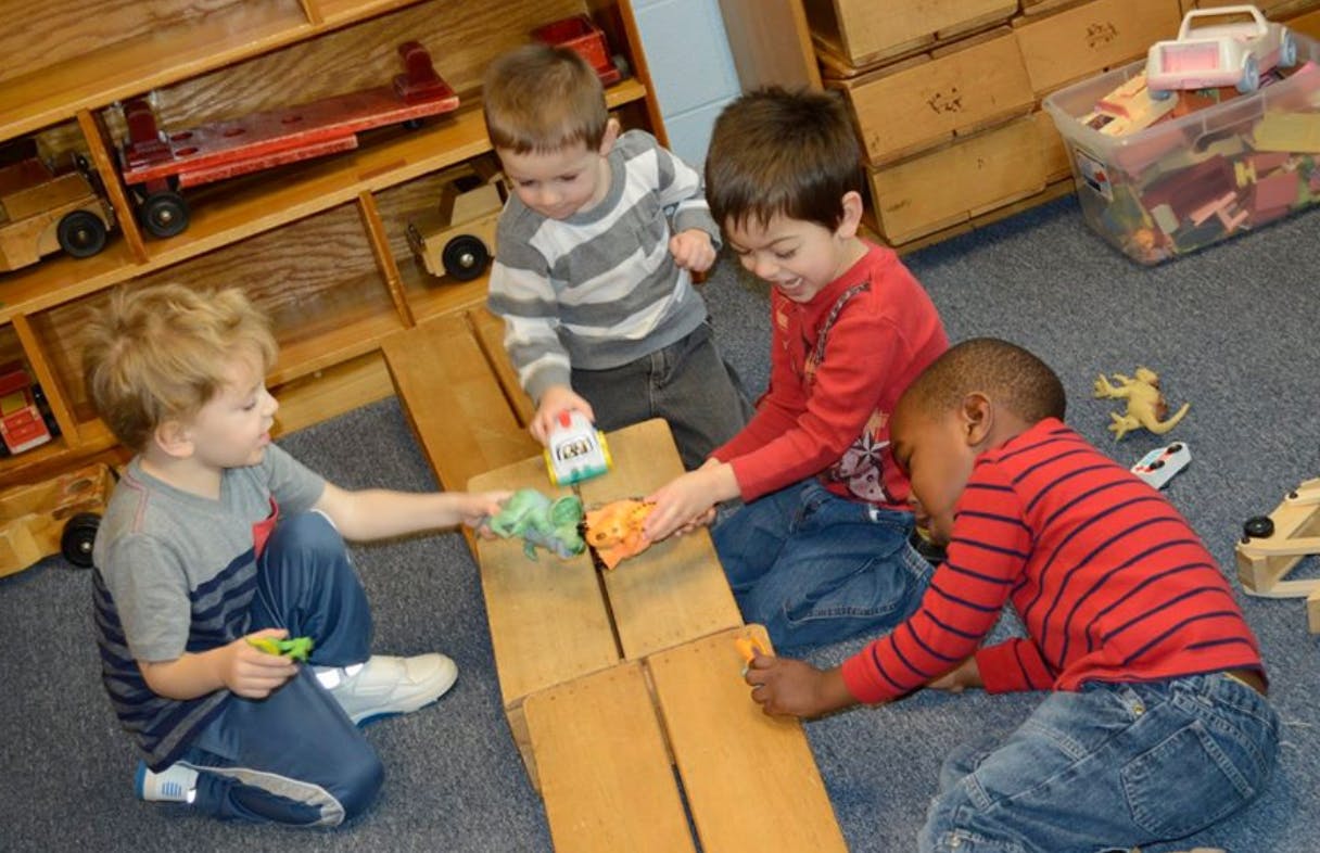 Four children playing with toy cars on wooden blocks in a classroom
