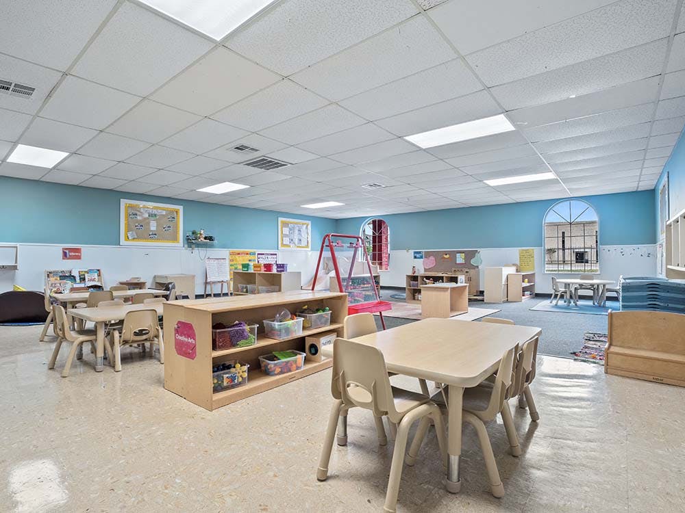 Empty children's classroom with small tables and shelves of supplies