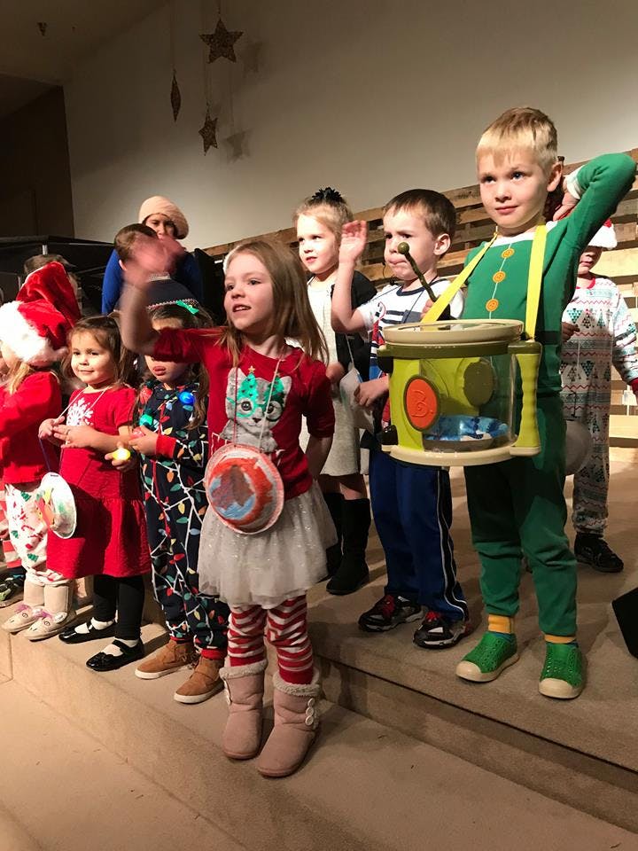 Children standing on a stage, some waving