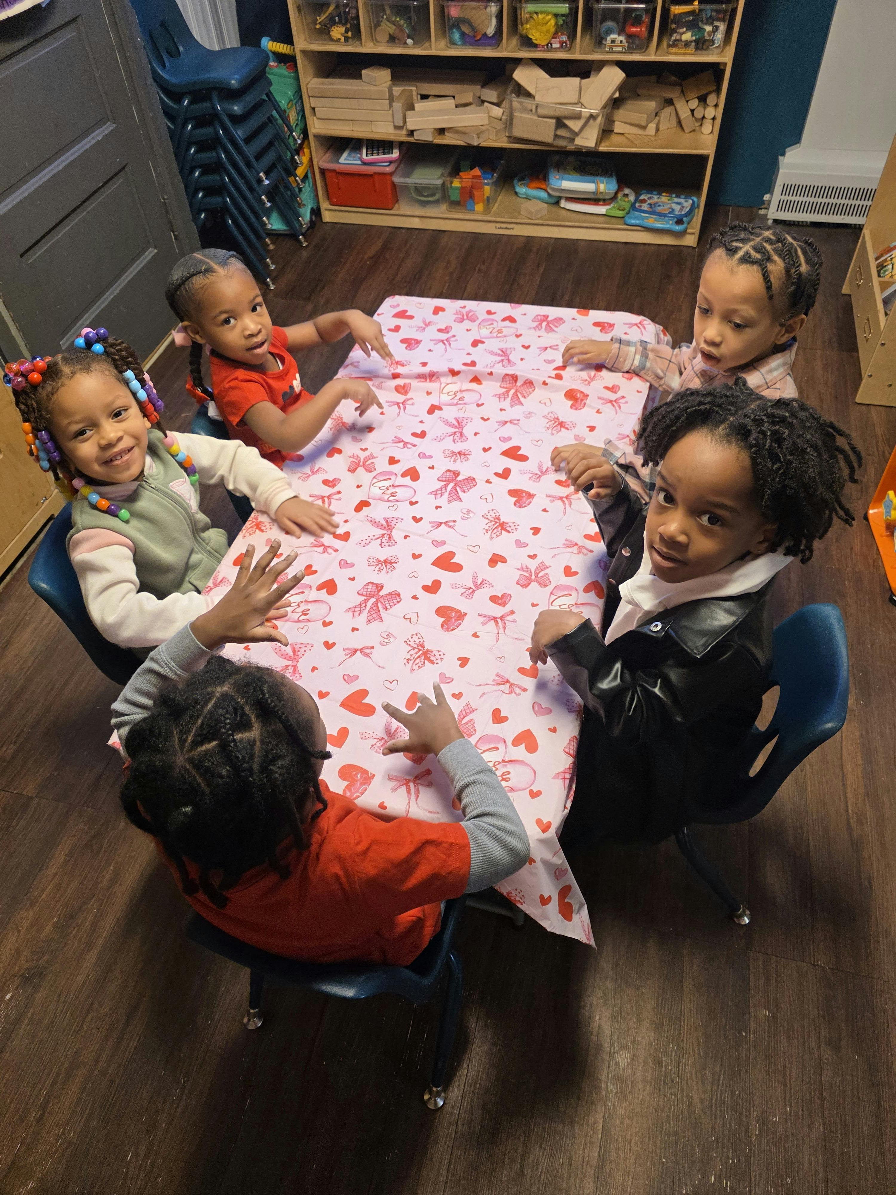 Five children sitting around a table with a heart-patterned tablecloth