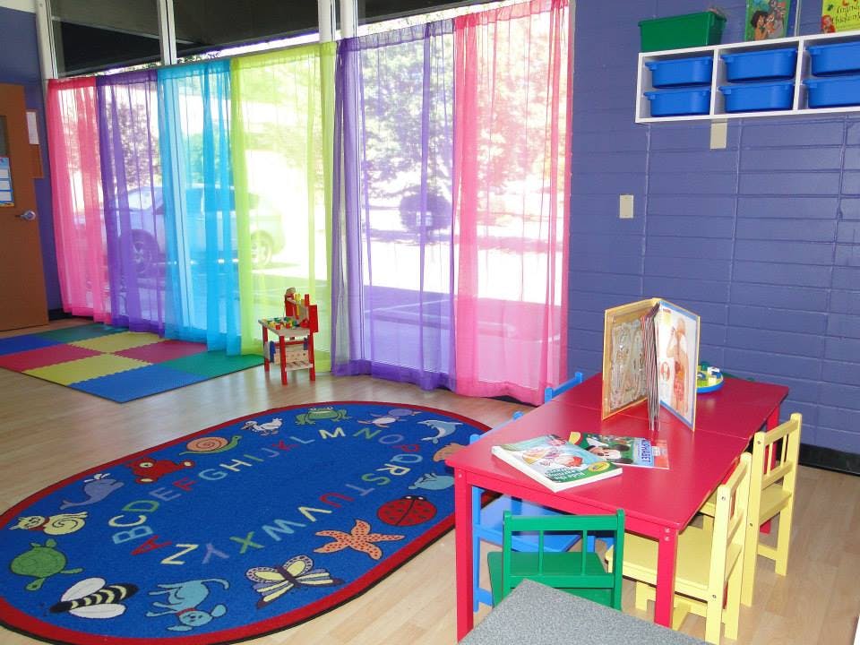 Classroom with colorful curtains, alphabet rug, and small red table with chairs