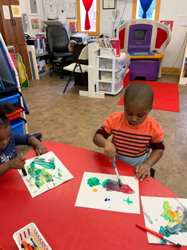 Two children painting at a red table in a classroom