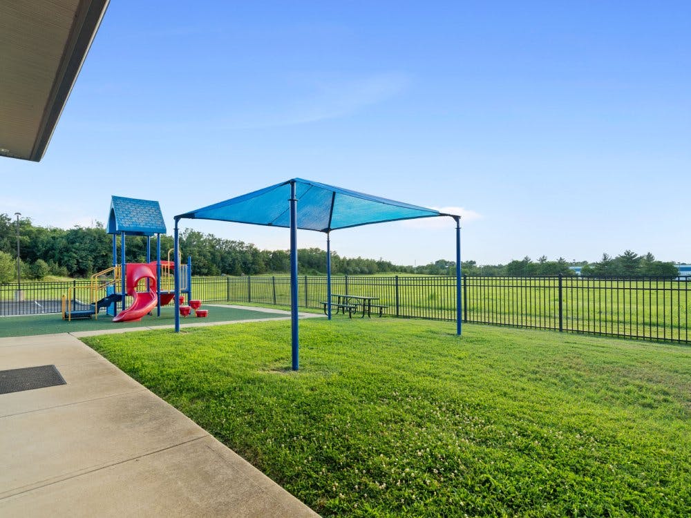 Playground with red slide, blue canopy, and green grass
