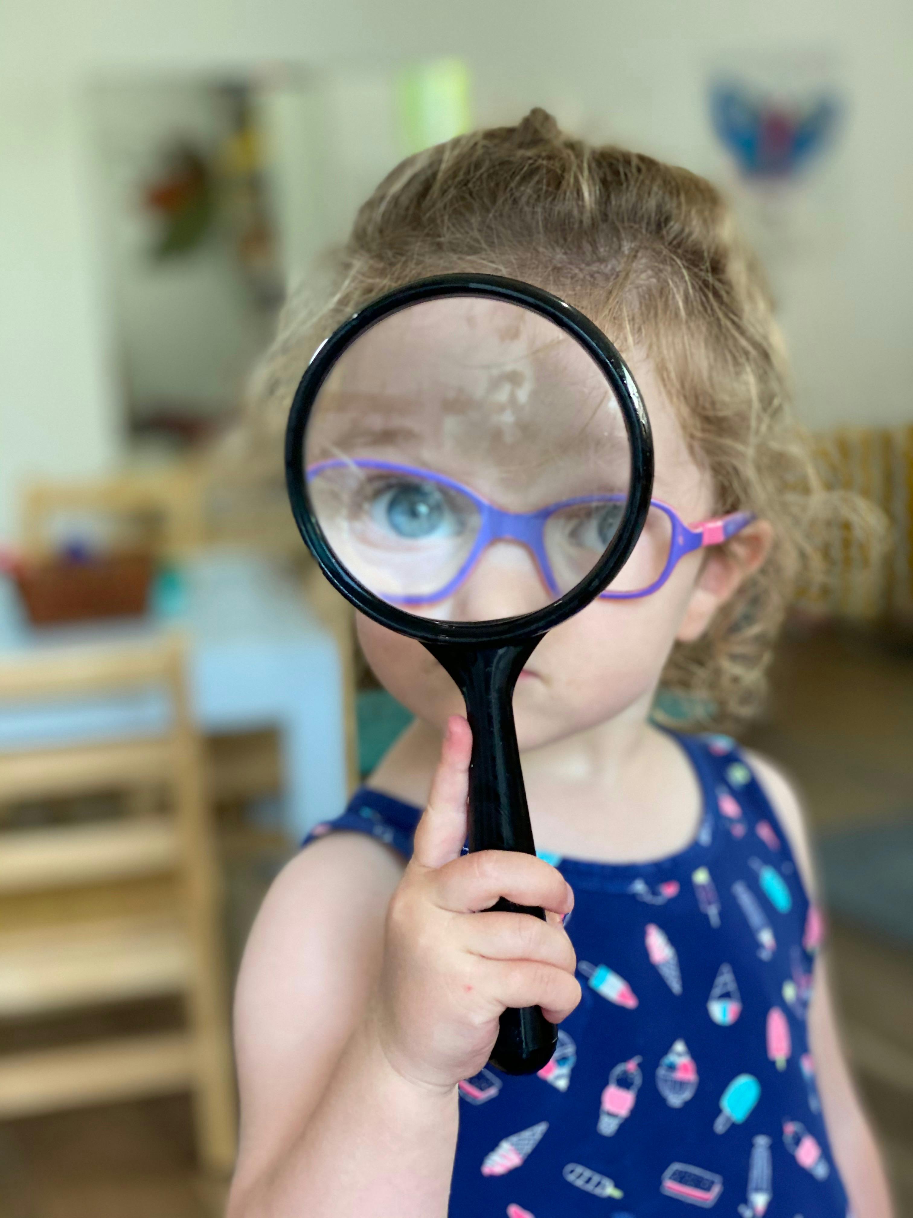 Child holding a magnifying glass to their face