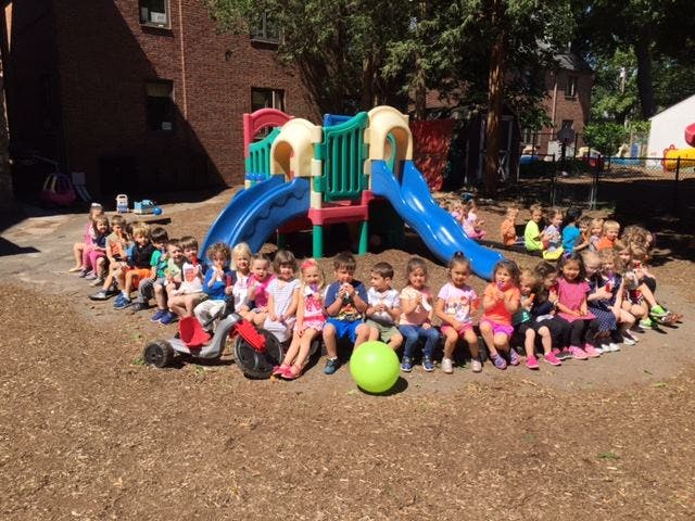 Children sitting in a line on a playground with a slide structure