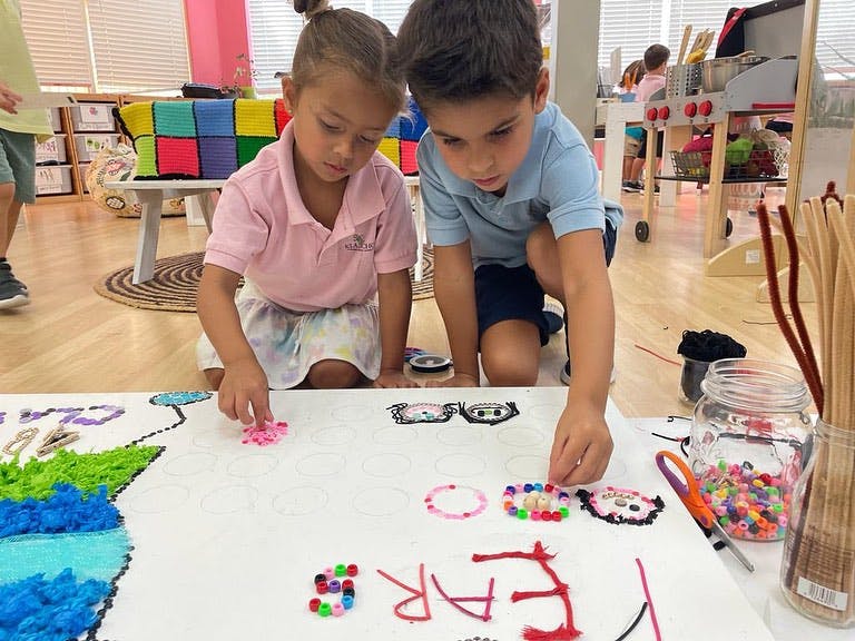 Two children kneeling and placing small objects on a large white sheet of paper