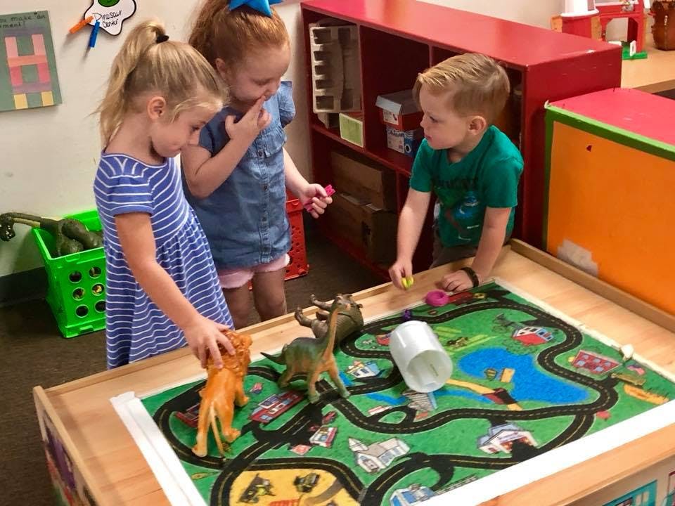 Three children playing with toys on a mat with roads and water