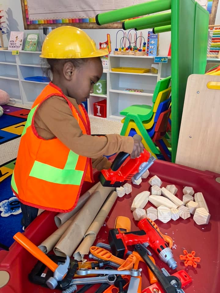 Child in hard hat and safety vest playing with toy tools
