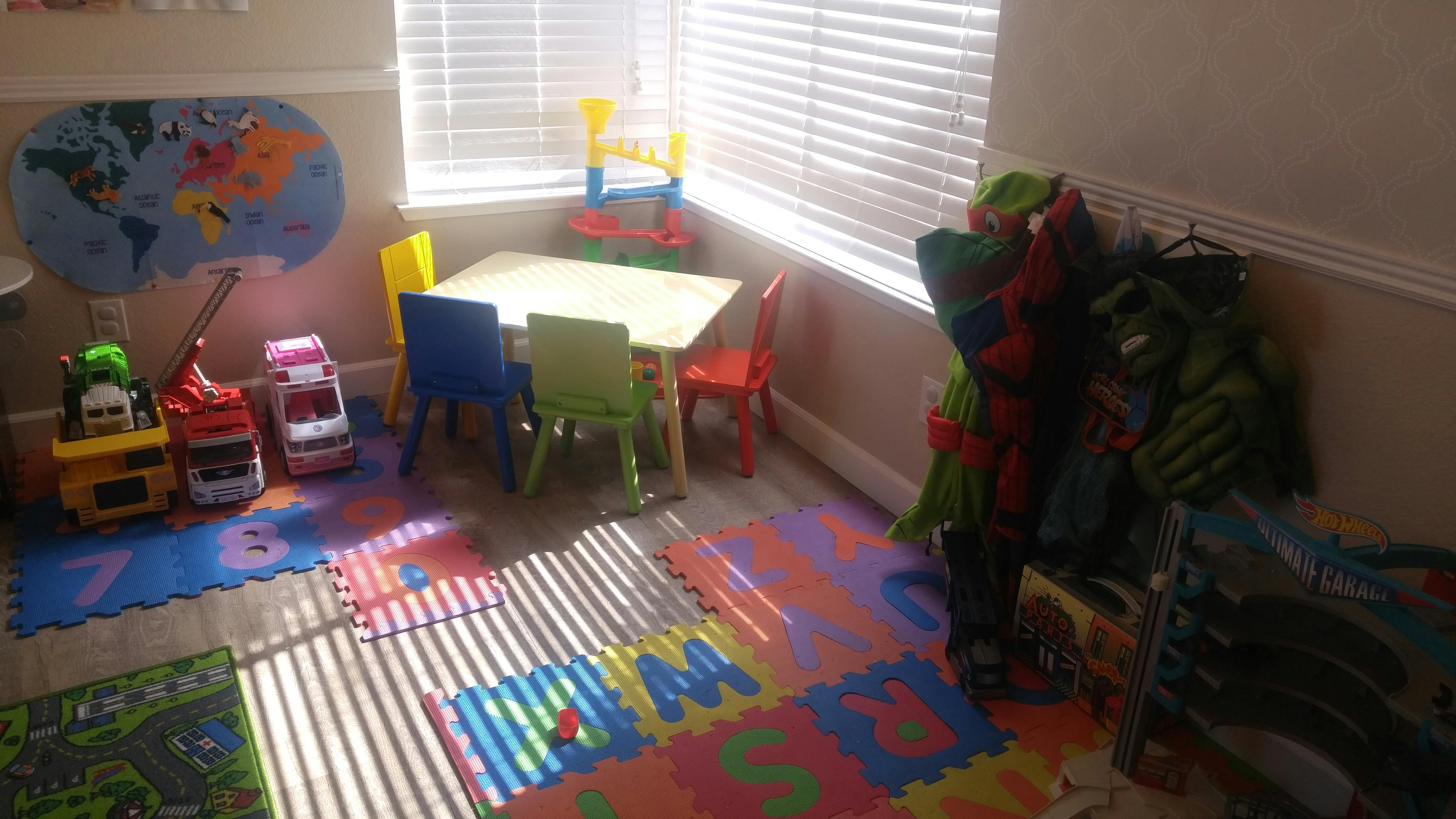 Playroom with small table and chairs, alphabet floor mats, and toys