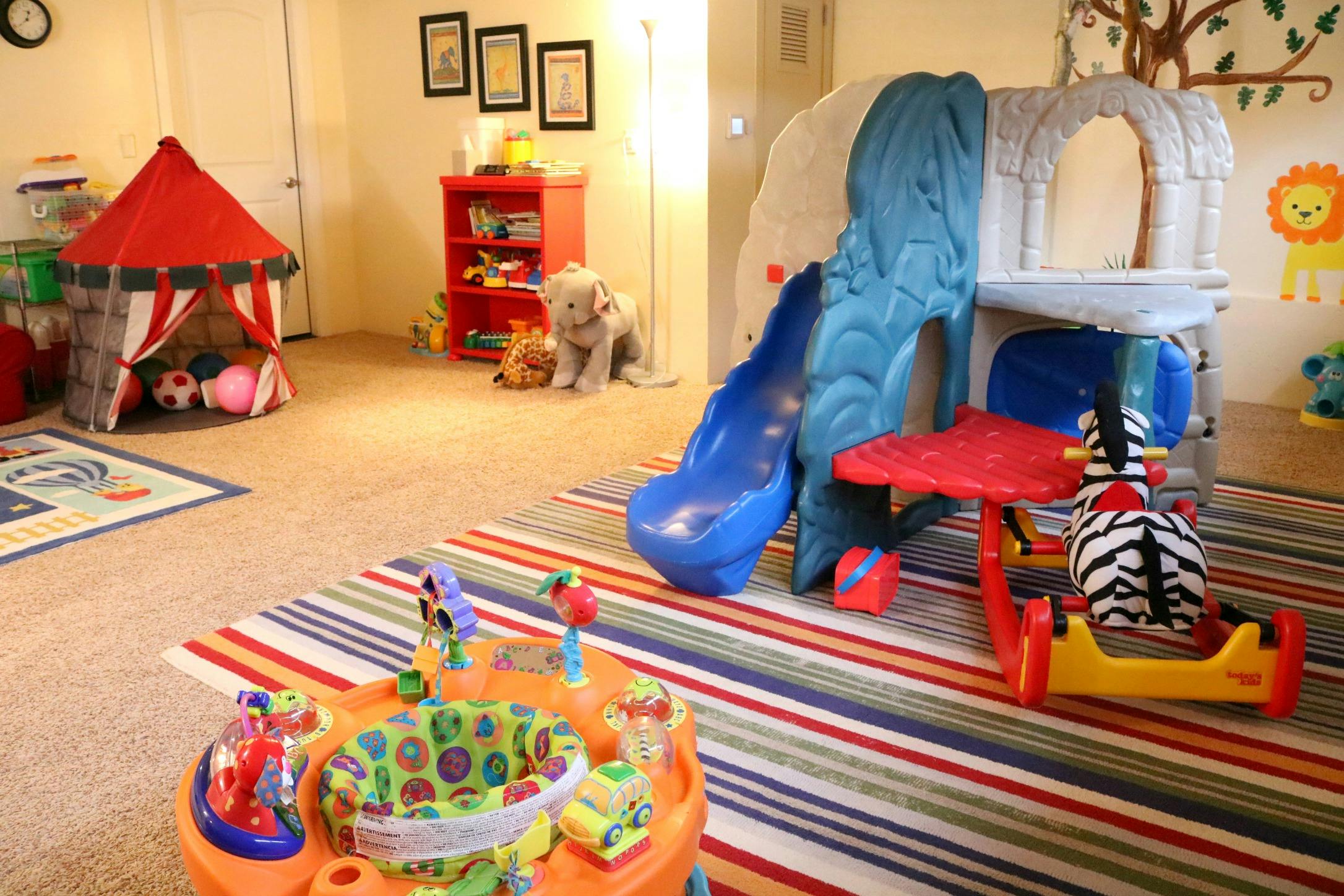 Playroom with a red tent, blue slide, and activity center