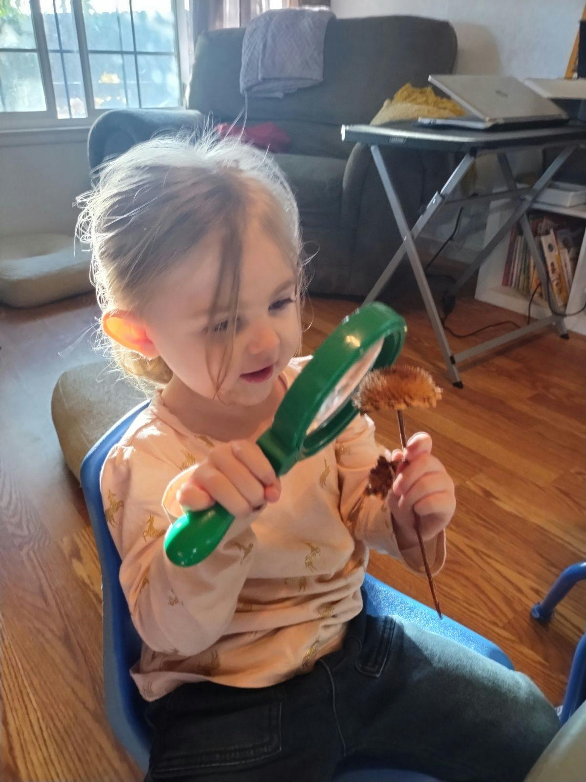 Child holding a magnifying glass and a stick with a pinecone