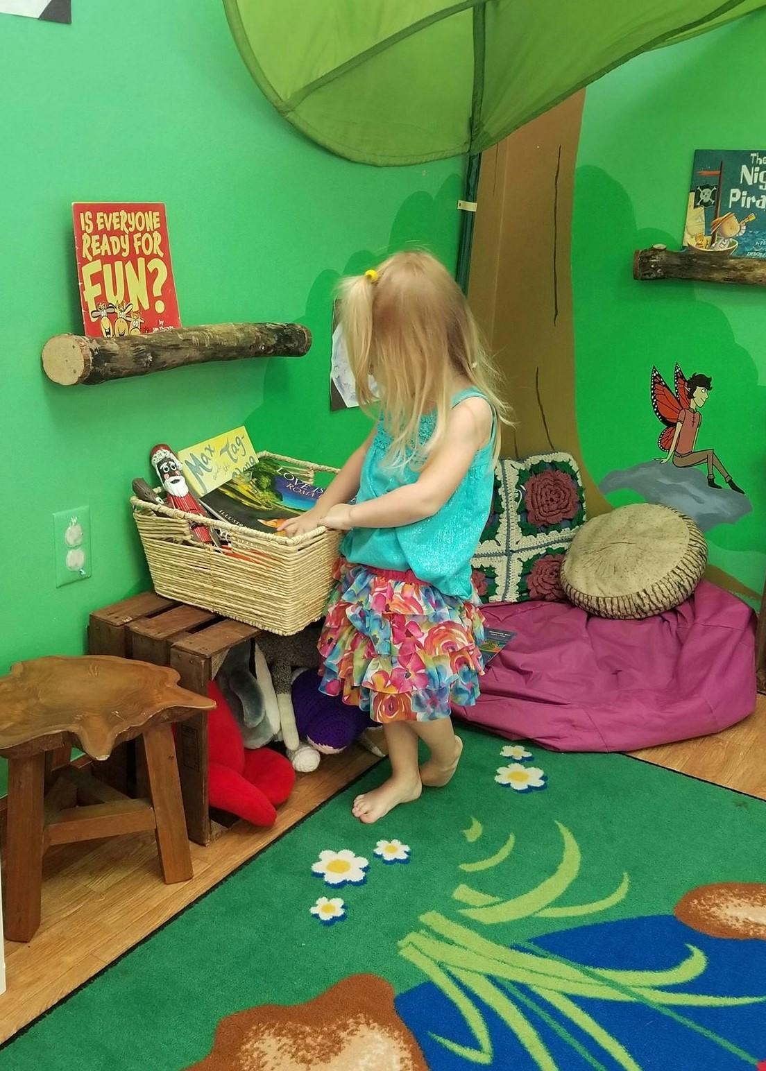 Child standing in a play area, looking into a basket