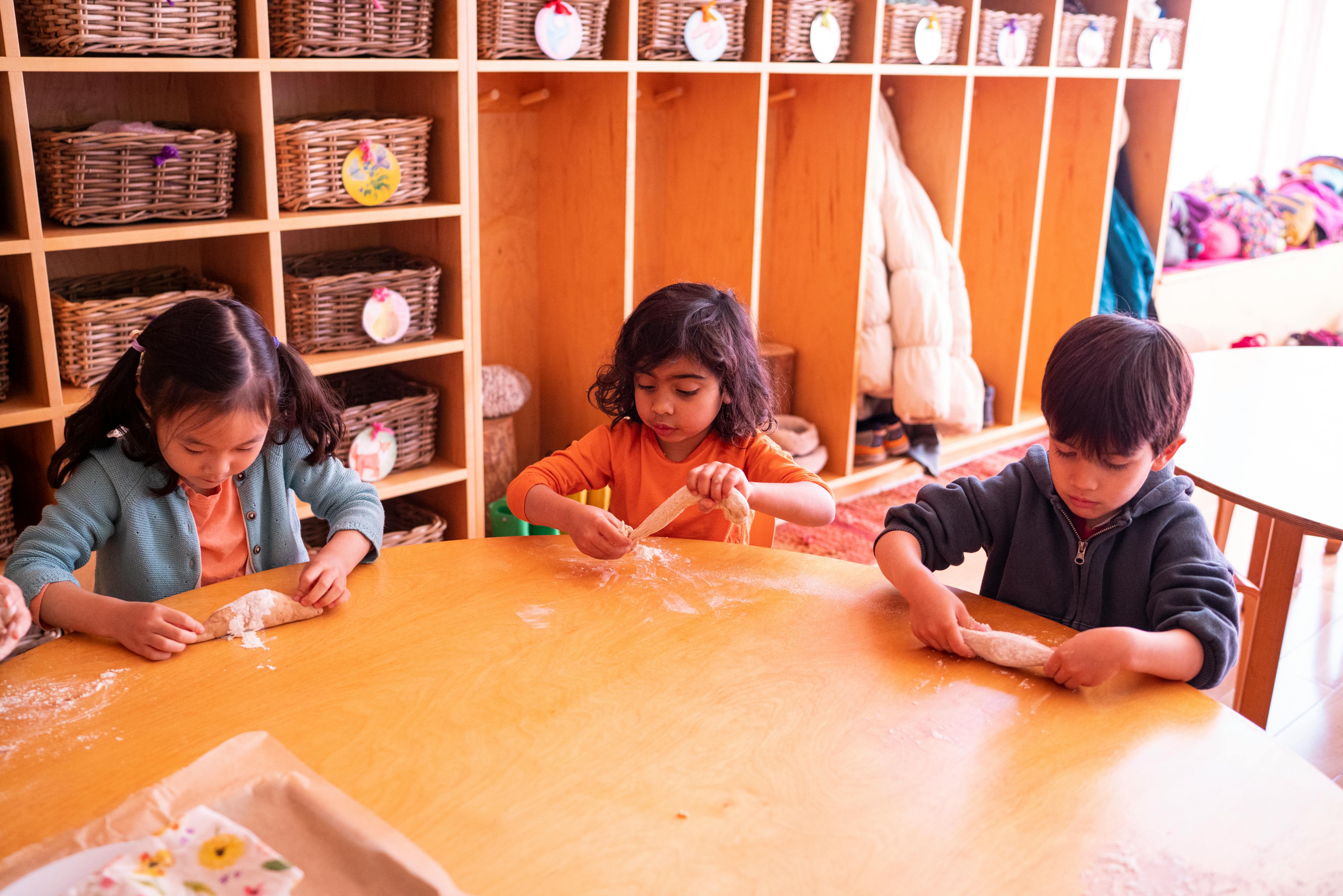 Three children at a table making dough in a classroom
