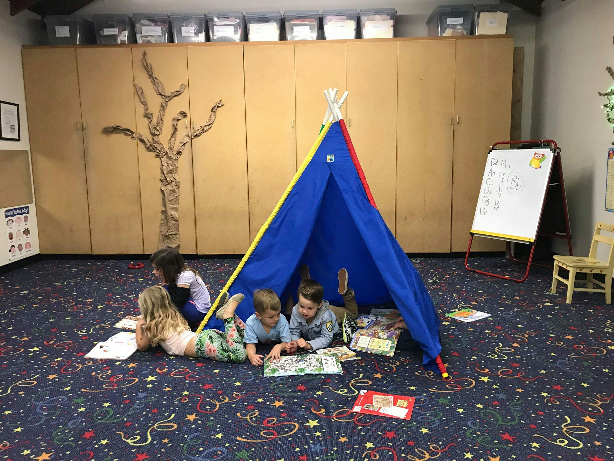 Children reading books around a blue play tent