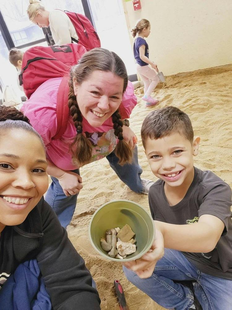 People holding a bucket of rocks in a sand pit
