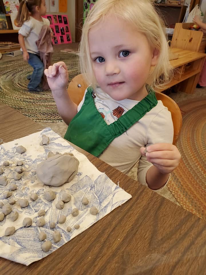 Child in green apron making small clay balls at a table