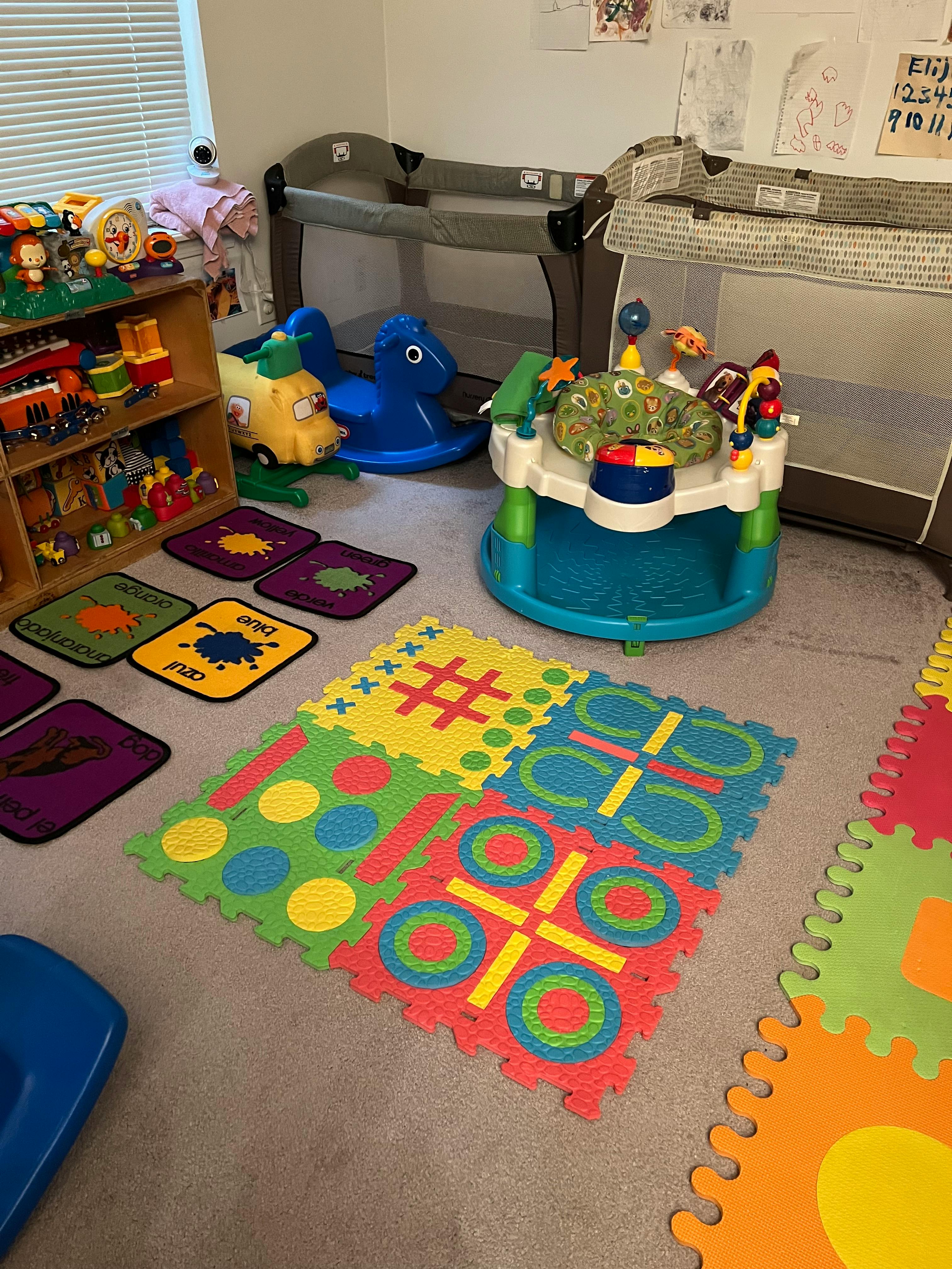 Playroom with cribs, toys, and colorful floor mats