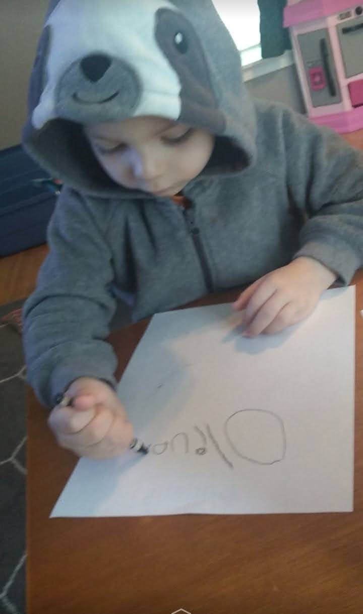 Child in a hooded sweatshirt drawing on paper