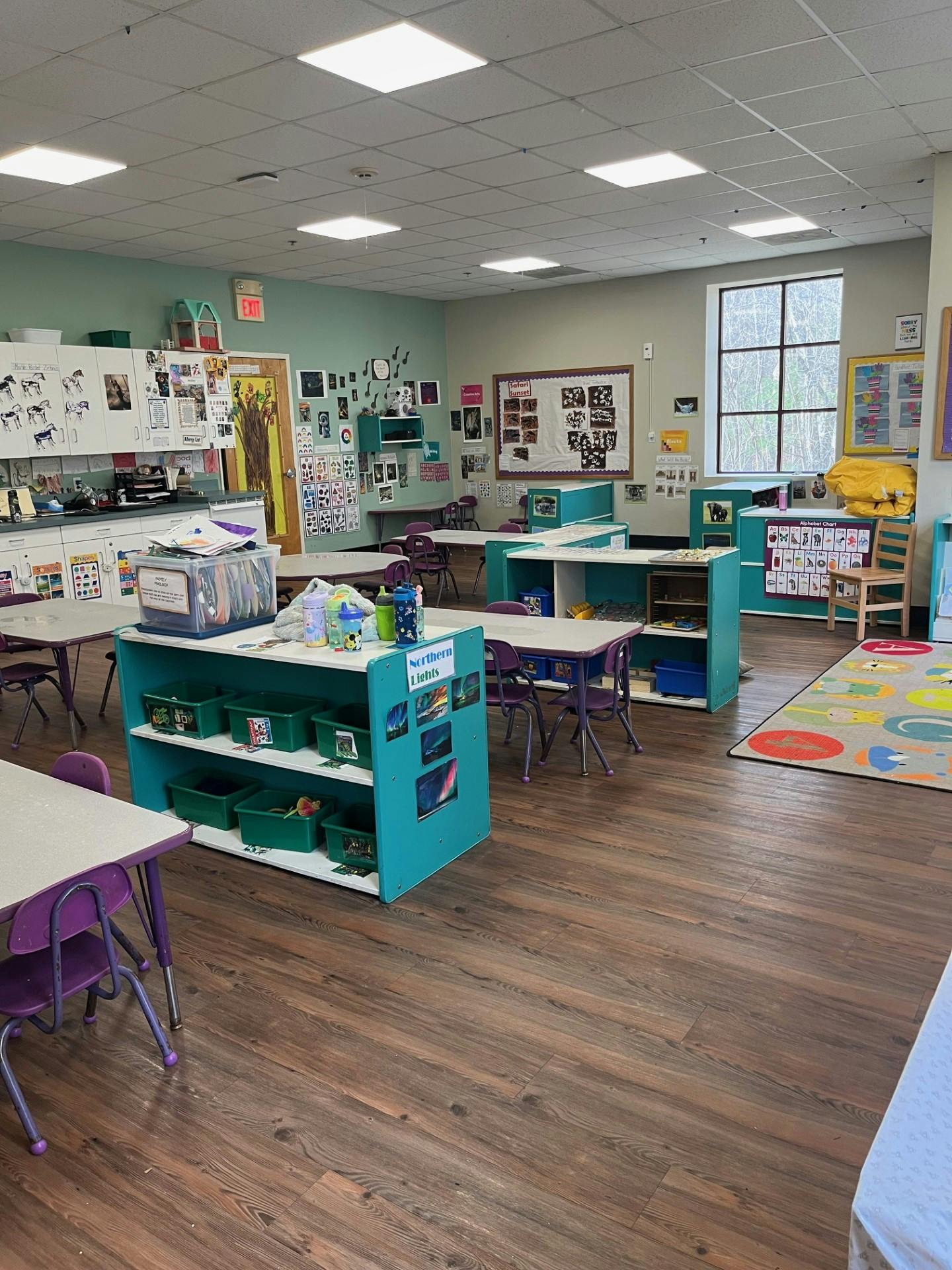 Empty classroom with small tables and chairs, storage units, and decorated walls