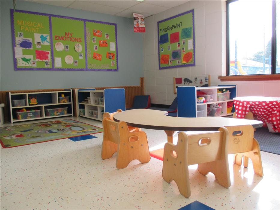 Classroom with low tables and chairs, shelves of toys, and colorful bulletin boards