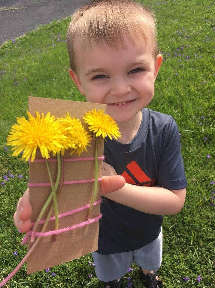 Child holding a cardboard tube with dandelions attached by pink rubber bands