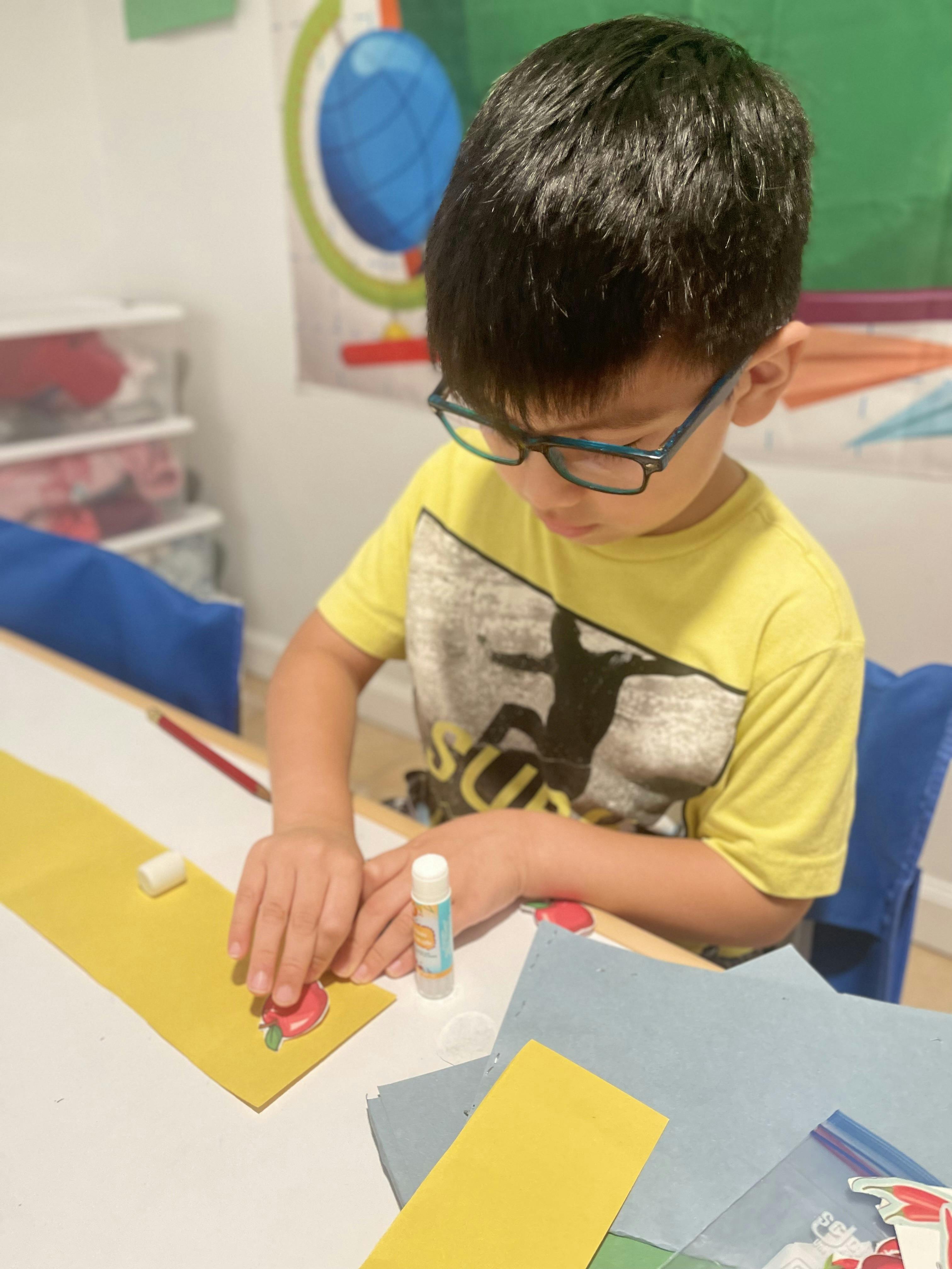Child in glasses crafting with paper and a glue stick
