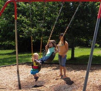 Two children and one teen on swings at a playground