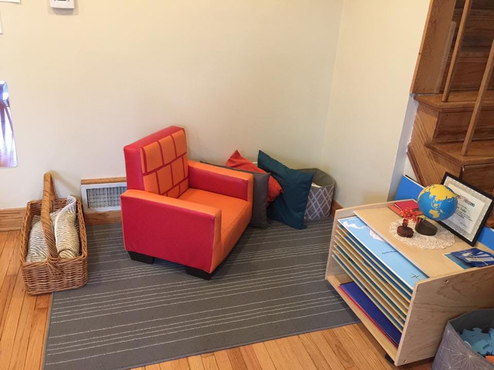 Small red and orange armchair on a rug next to a basket and a small table with a globe