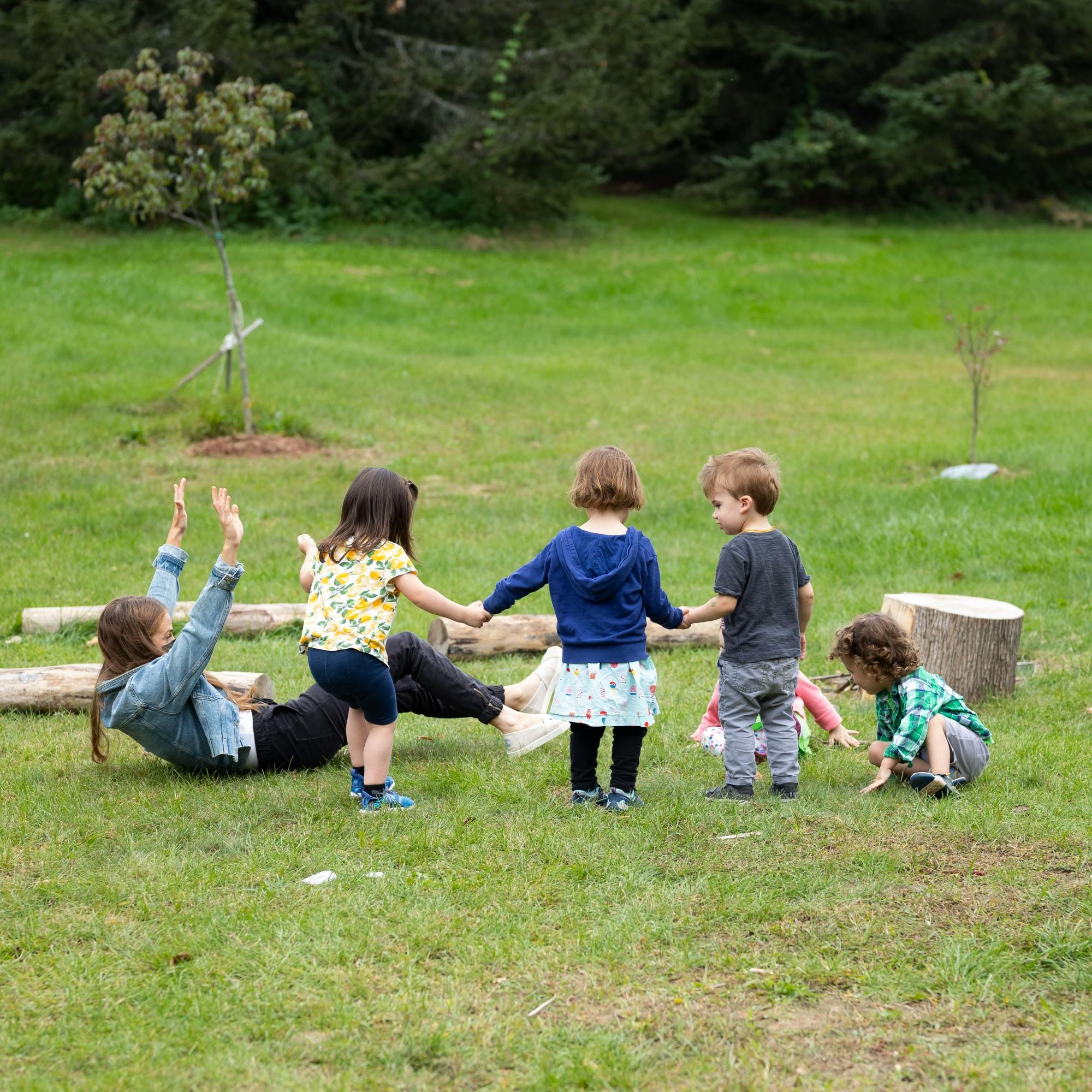 Person on grass with arms up, surrounded by four children holding hands