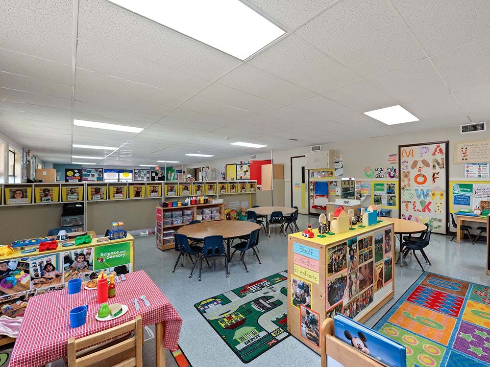 Empty colorful preschool classroom with small tables, chairs, and play areas