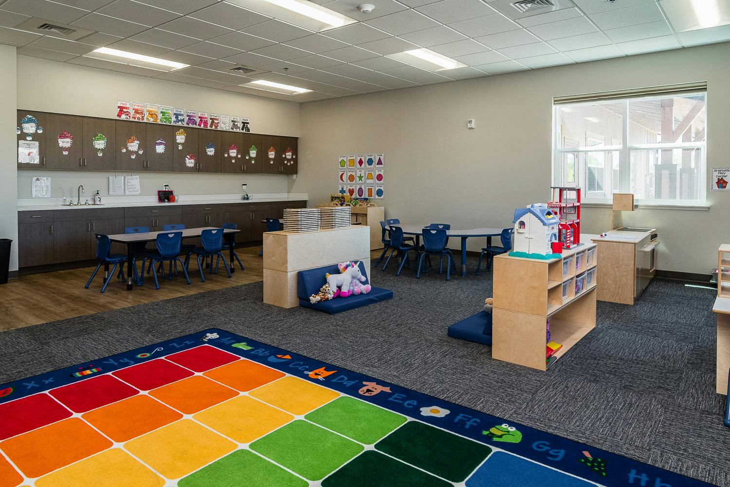 Empty classroom with a colorful rug, tables, chairs, and shelves